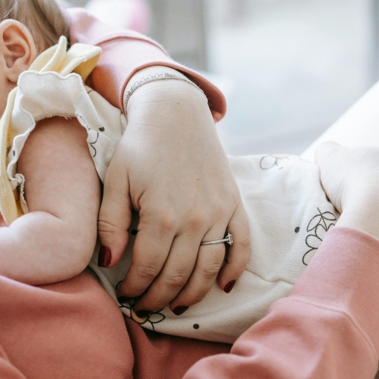 contact dutje babyslaap Een moeder houdt een baby gekleed in een lichte romper vast, met een zachte achtergrond.